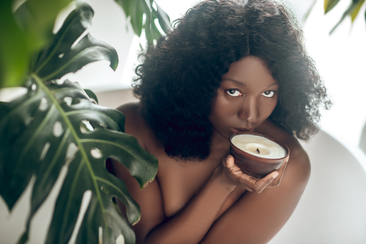 Naked dark-skinned woman smelling an organic candle