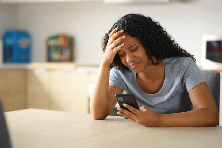Sad woman checking phone in the kitchen at home