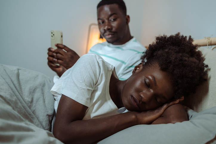 Young woman is sleeping while her partner is using smart phone in bed