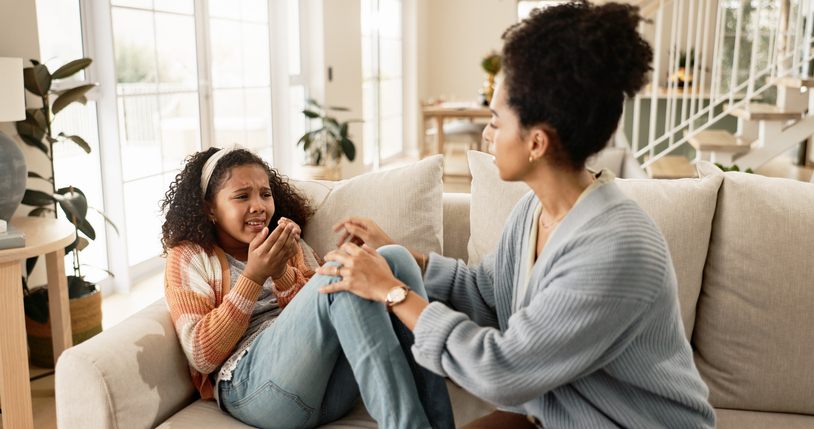 Mom, sad and comfort girl on sofa with kindness, empathy and listening to trauma in living room at house. Crying, African mother and daughter with support, love and console in lounge at family home