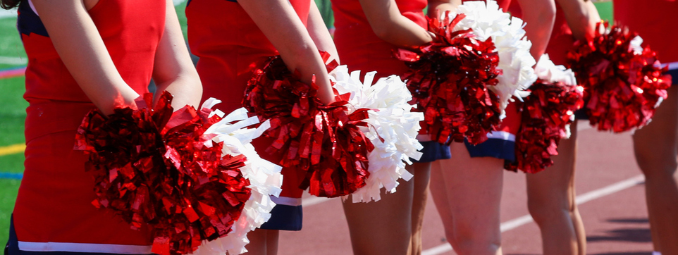 Cheerleaders standing on the sideline holding pom poms behind them