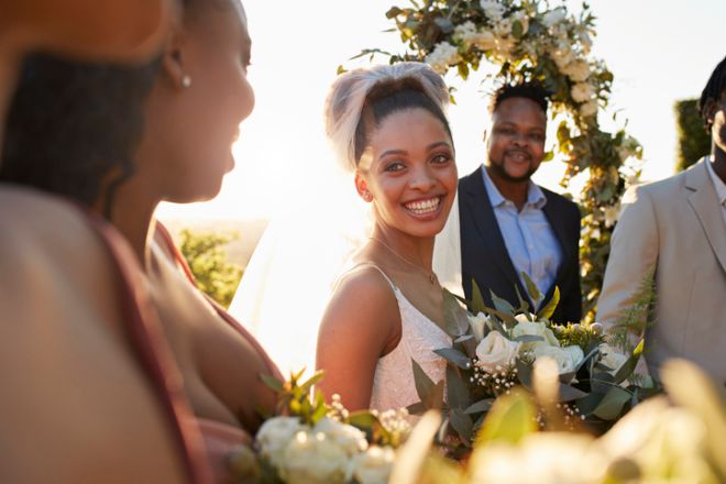 Happy young bride holding bouquet looking at bridesmaids