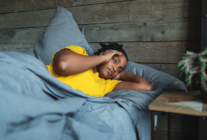 Depressed frowning young adult black woman with headache lying in bed