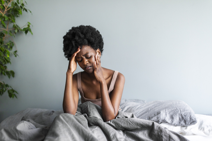 Depressed frowning young adult black woman with headache sitting in bed