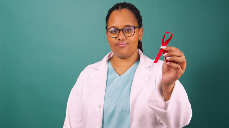Black female doctor holding red awareness ribbon, serious in white coat