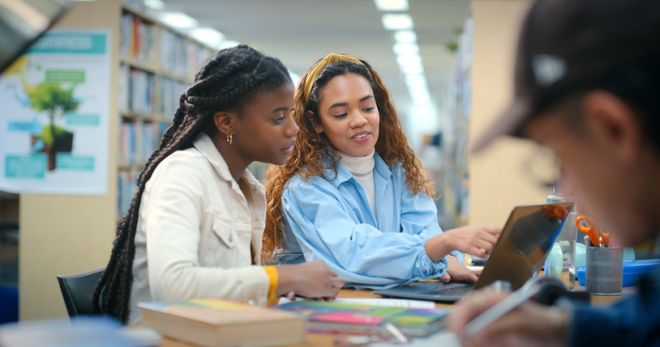 Students, women or help on laptop in library for advice, information or college scholarship. School, teamwork or people learning on pc for research, solution or study for online test in university