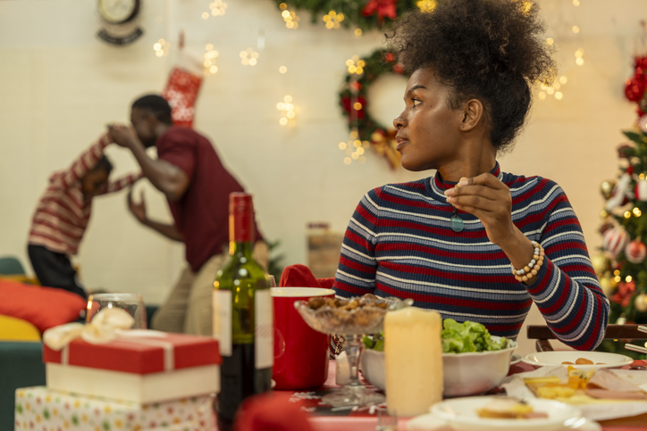 A joyful family gathers around the dinner table celebrating Christmas. The father, dressed in a Santa hat, gives a gift to the child, while everyone smiles with warmth and festive decorations.