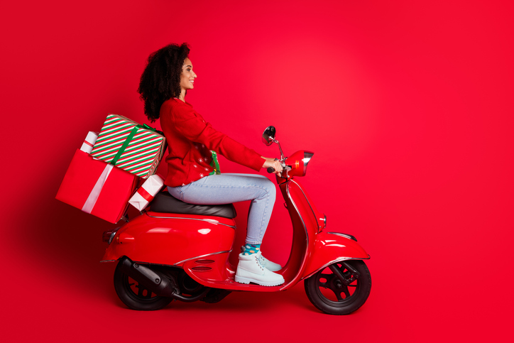 Profile side photo of lovely charming girl wear sweater deliver xmas gift ride scooter magic miracle isolated on red color background