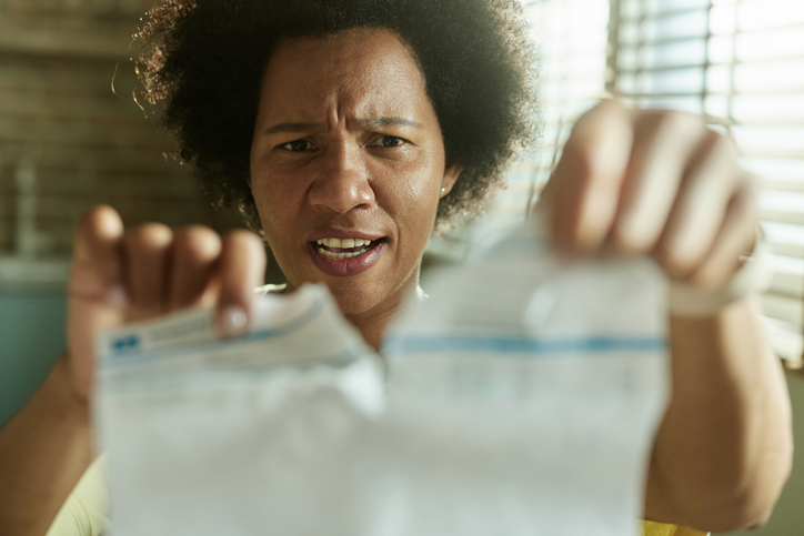 Displeased black woman tearing financial bill at home.