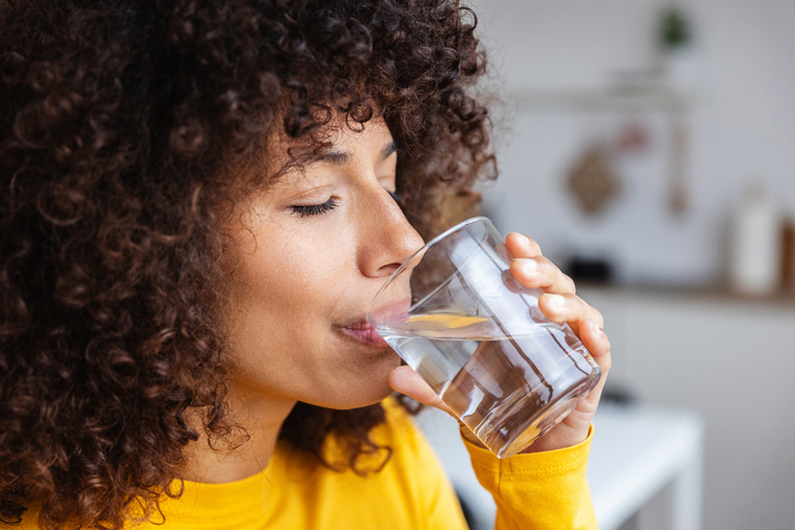 Young woman drinking fresh water from a glass in the kitchen at home