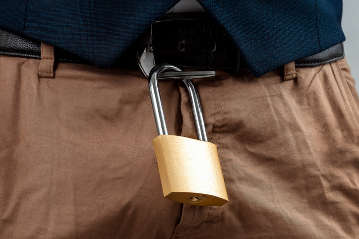 Close-up of a gold padlock hanging from a man's belt. The concept of marital fidelity, celibacy, treason, abstinence chastity belt.