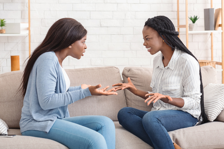 Two girlfriends sitting on sofa and arguing with each other
