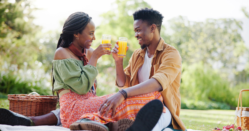 Nature, picnic and black couple toast with juice on blanket for bonding, relationship and trust outdoors. Dating, drinks and man and woman on weekend for romance, anniversary celebration and love