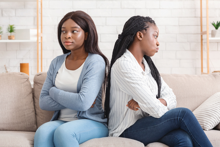 Two offended afro girlfriends sitting back to back on sofa