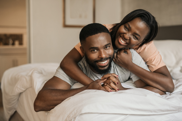 Smiling young African American couple playing in bed together