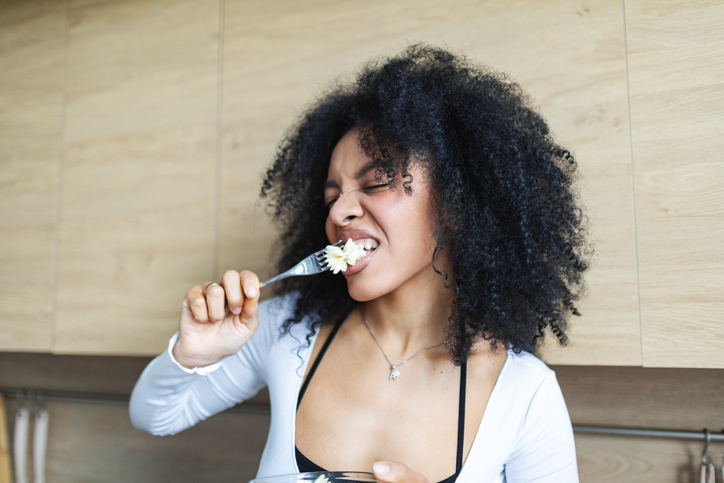 Young adult woman eating pasta salad, having fun and grimacing