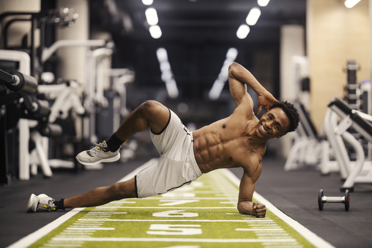 Fit shirtless black sportsman doing workouts for abs in a gym.