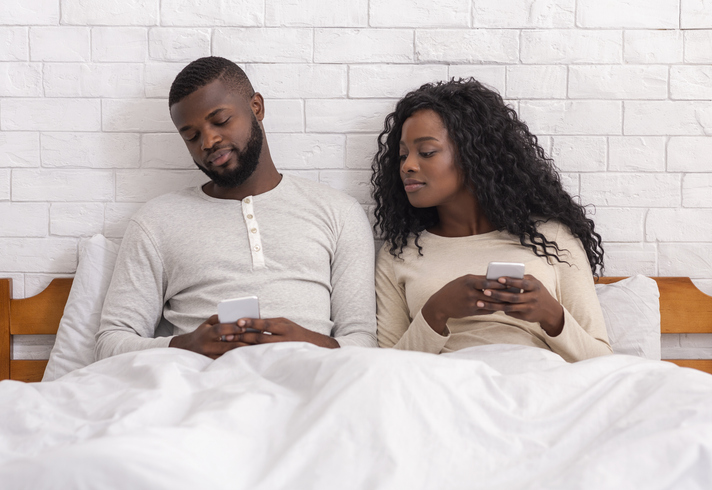 Jealous man peeking into wife's cellphone sitting on bed together, relationship