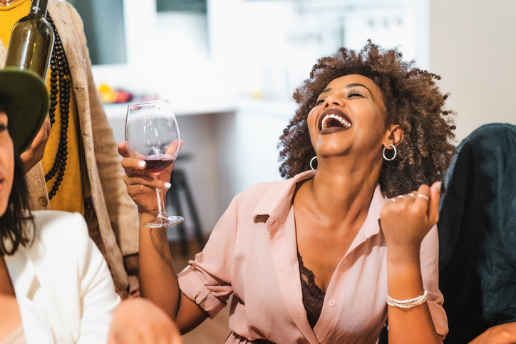 Portrait of an African American woman laughing drinking wine sitting with her friends dining at multiethnic party
