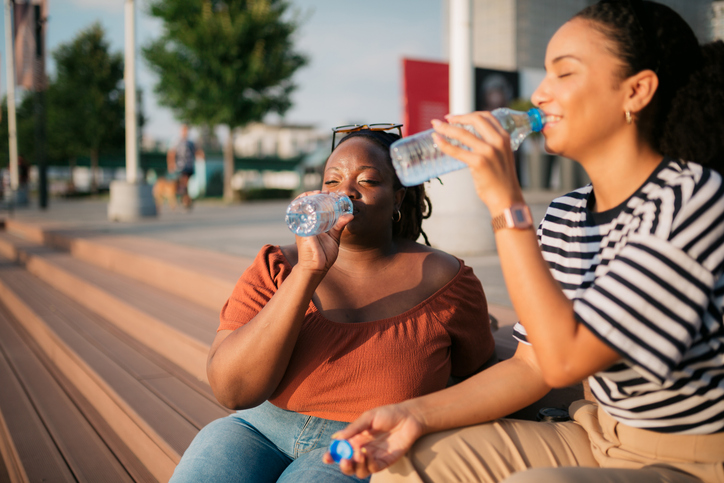 Two woman friends drinking water sitting on city steps