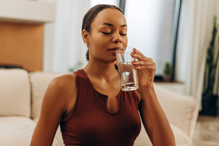 Beautiful African American sporty woman going to drink water sitting at home