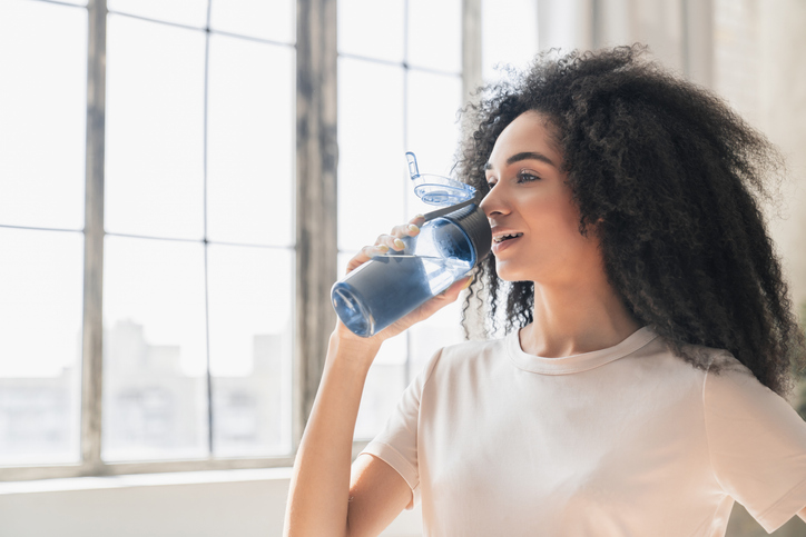 Happy black woman with water bottle for hydration in health and wellness at home.