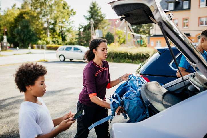 Mother Putting Rucksacks In Car Trunk After Hiking With Sons