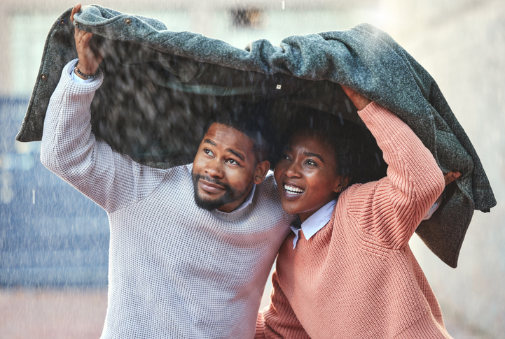 Shot of a young man and woman holding a jacket over their heads on a rainy day in the city