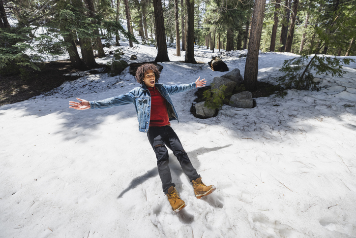 Young man with arms outstretched falling on snow in forest