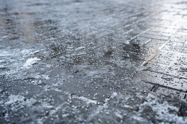 Deicing chemicals on pavement in winter. Salt grains on icy sidewalk paving slab with technical salt
