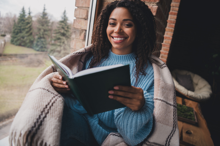 Smiling woman reading a book near large window in cozy living room on a relaxing autumn afternoon