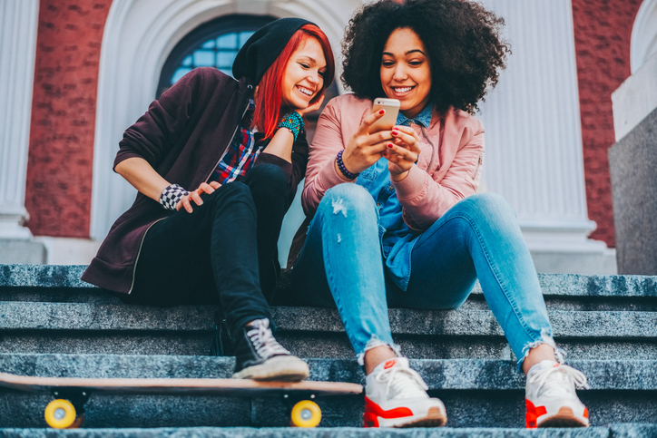 Young girls relaxing on urban steps with smartphones and skateboard