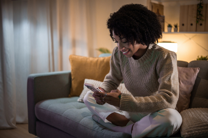 Young woman relaxing on sofa using smartphone at night