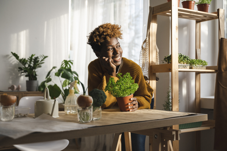 Happy woman with potted plant leaning on table at home