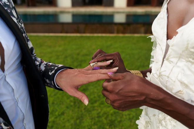 Ambiguous gender fluid couple in white dress, bold suit exchange rings at tropical villa. Fresh lgbtq wedding setting. The bride elegance meets groom style.