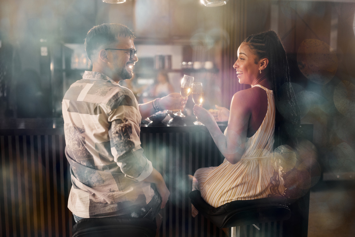 Cheerful couple toasting with champagne at bar counter at home.