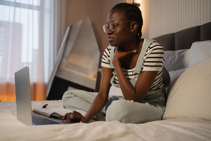 Young african american woman working from home using laptop in bed