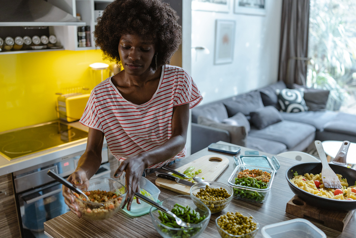 African American young woman preparing homemade meals for storage in containers on the kitchen counter