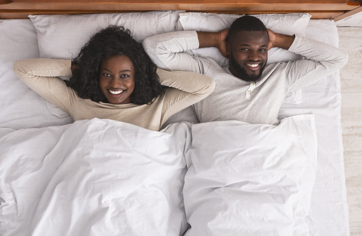 Satisfied couple resting in bed with hands behind the head