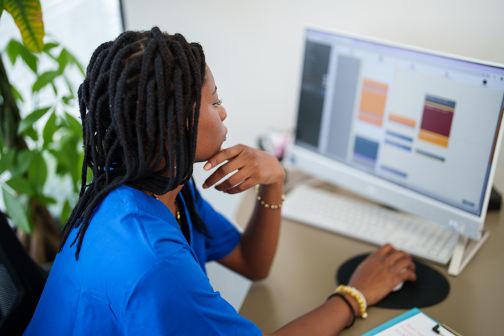 Woman with blue scrubs working on medical record on computer.