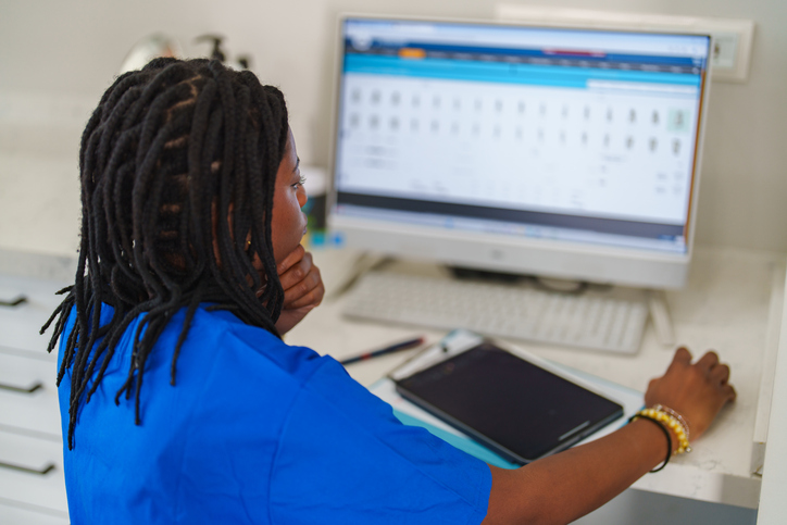 Woman with blue scrubs working on medical record on computer.