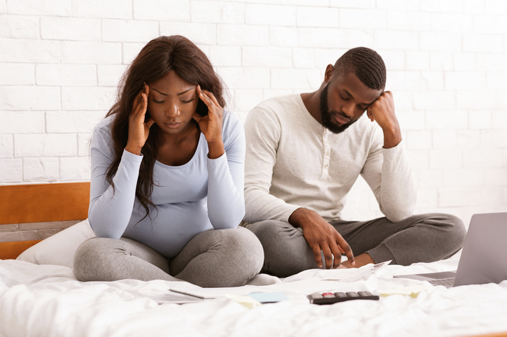 Sad pregnant couple planning budget, sitting on bed at home