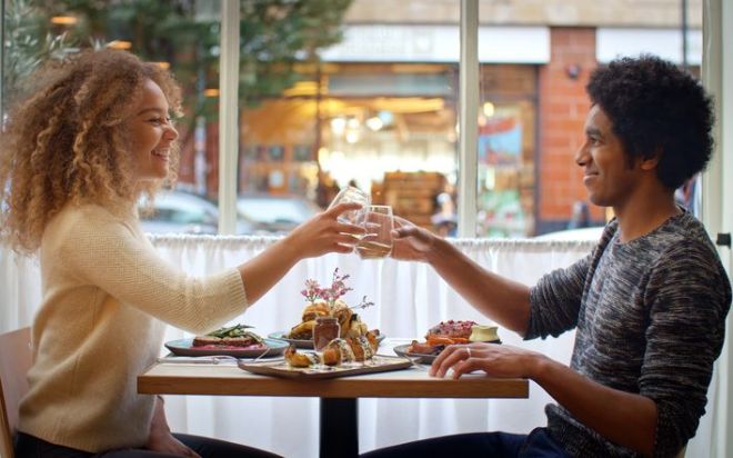 Young Couple Doing Cheers With Drinks Enjoying Meal On Date In City Restaurant Together