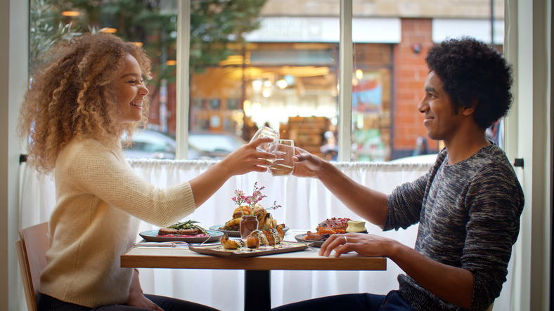 Young Couple Doing Cheers With Drinks Enjoying Meal On Date In City Restaurant Together