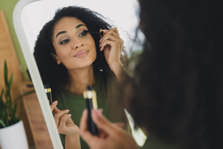 Photo of attractive young woman apply mascara mirror reflection dressed green outfit daylight home interior living room