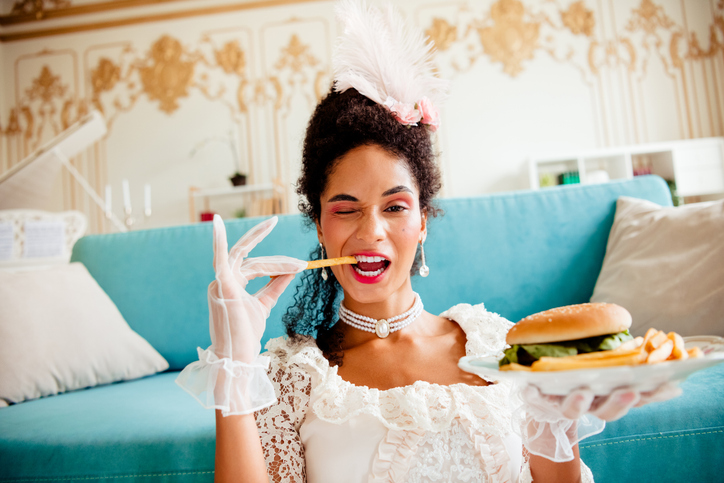 Elegant Young Woman in Historical Dress Enjoying Modern Fast Food in a Luxurious Indoor Setting