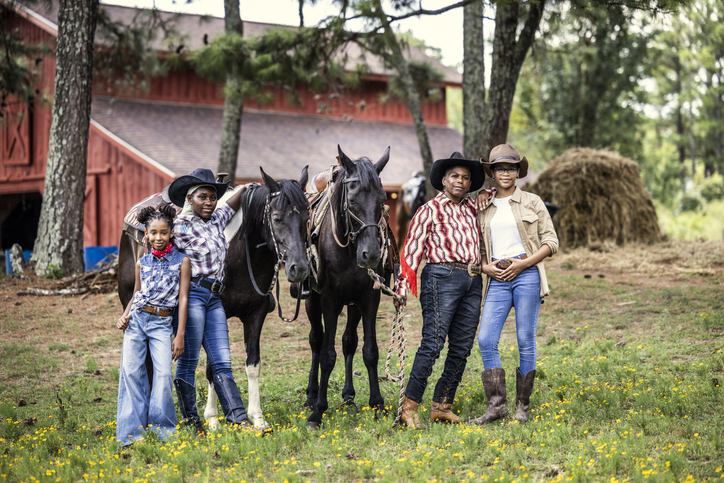 Portrait of multi-generational cowgirls in front of barn