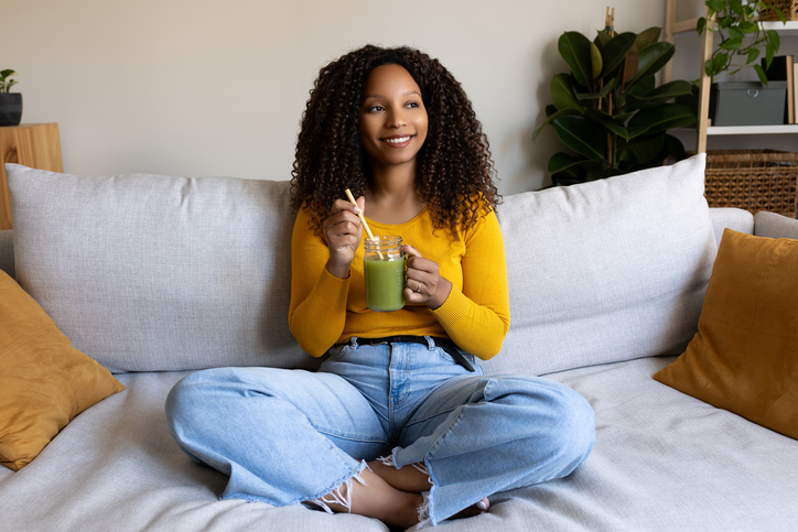 Young woman relaxing on sofa drinking green smoothie