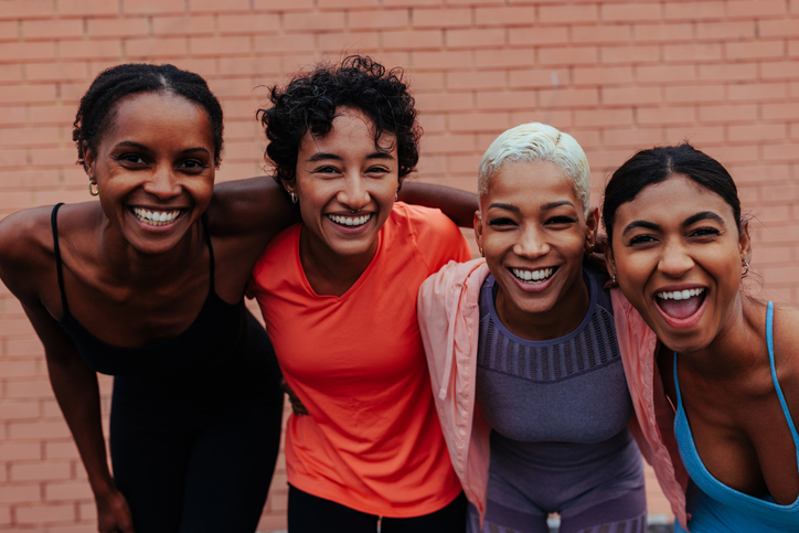 Four young women athletes smiling and hugging after training