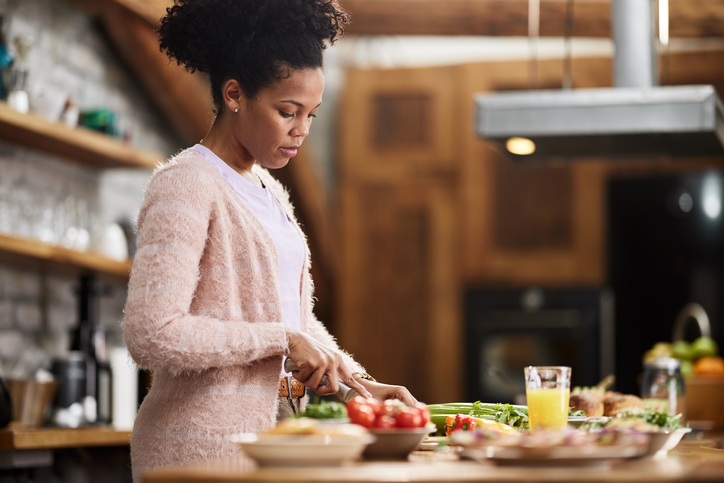 Young African American woman cutting vegetables for lunch.